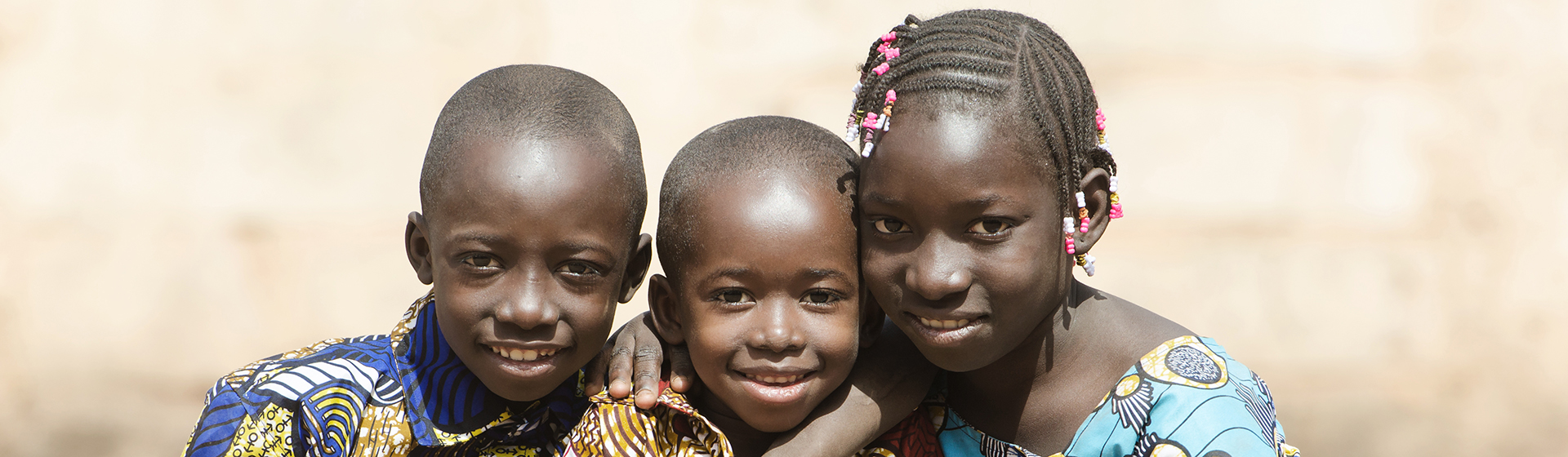 Three kids looking into the camera with their arms around each other and smiling.